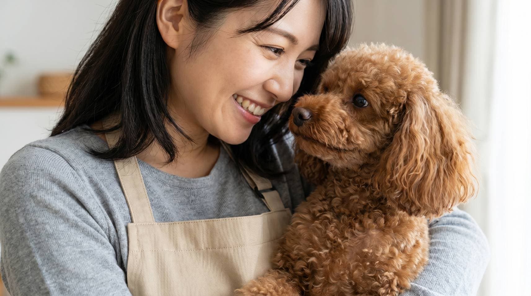 ペットシッターが笑顔でトイプードルを抱きしめている様子